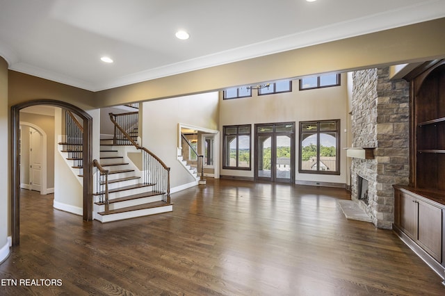 unfurnished living room with ornamental molding, dark wood-type flooring, french doors, and a stone fireplace