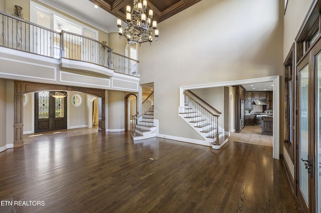 unfurnished living room with an inviting chandelier, a towering ceiling, french doors, wood-type flooring, and coffered ceiling