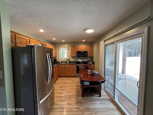 kitchen with light wood-type flooring, appliances with stainless steel finishes, and a textured ceiling