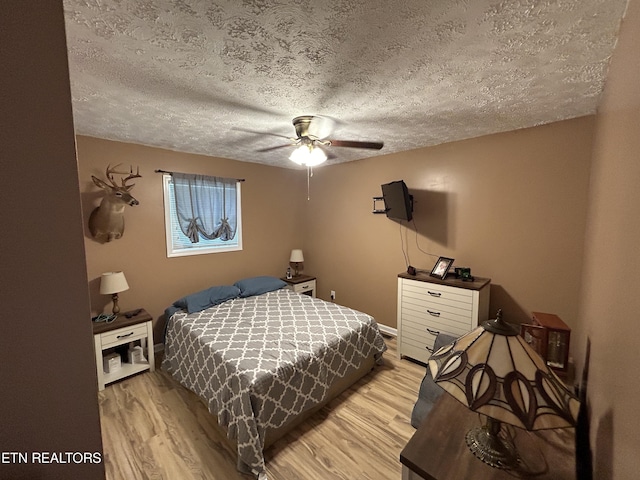 bedroom with light wood-type flooring, ceiling fan, and a textured ceiling