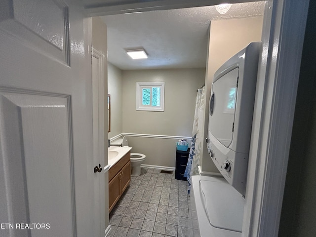 bathroom featuring stacked washer / drying machine, vanity, and toilet