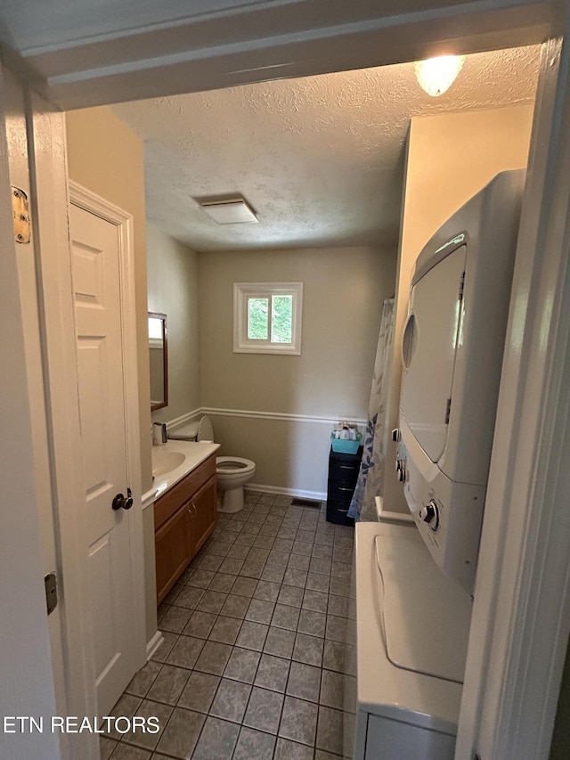 bathroom featuring stacked washer and dryer, toilet, tile patterned floors, a textured ceiling, and vanity