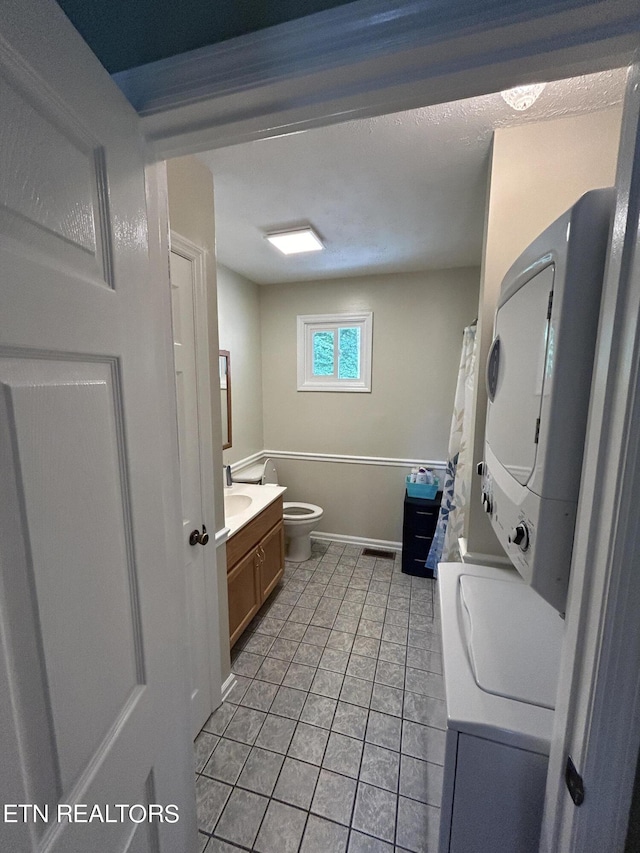 bathroom with stacked washing maching and dryer, toilet, tile patterned floors, and vanity