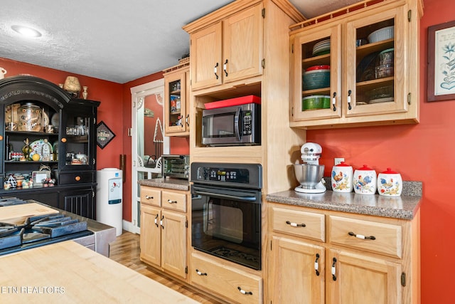 kitchen with black oven, light brown cabinets, and light hardwood / wood-style flooring