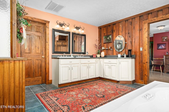 bathroom with wooden walls, tile patterned flooring, a textured ceiling, a washtub, and vanity