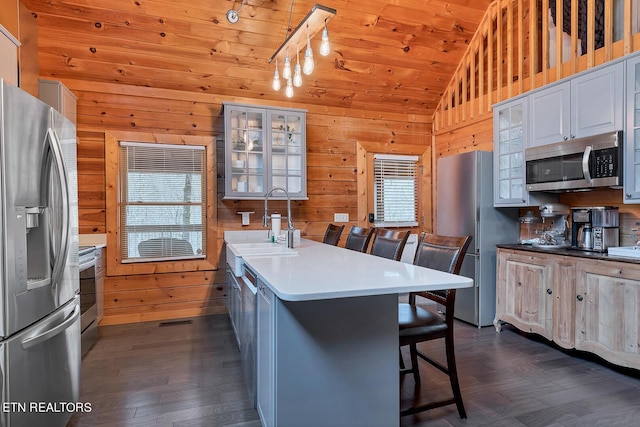 kitchen with a kitchen breakfast bar, stainless steel appliances, dark hardwood / wood-style floors, plenty of natural light, and wood walls