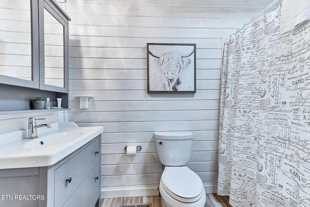 bathroom featuring walk in shower, toilet, wooden walls, vanity, and hardwood / wood-style flooring