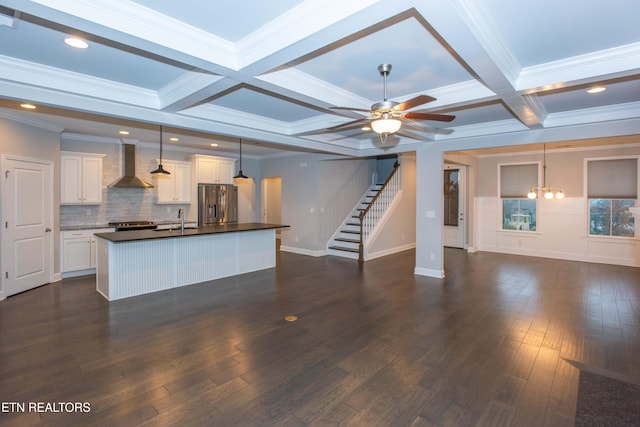 kitchen featuring dark countertops, beamed ceiling, stainless steel fridge, wall chimney exhaust hood, and a sink