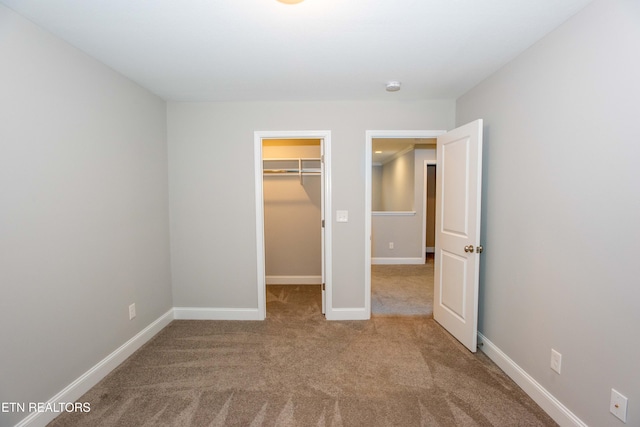 unfurnished bedroom featuring a walk in closet, carpet floors, baseboards, and a closet