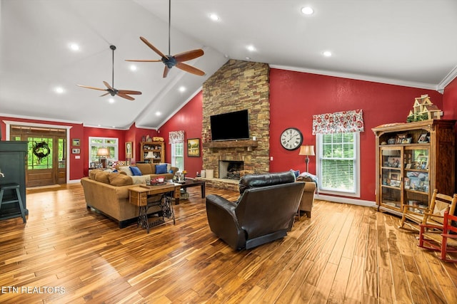 living room featuring ceiling fan, crown molding, high vaulted ceiling, light hardwood / wood-style flooring, and a stone fireplace