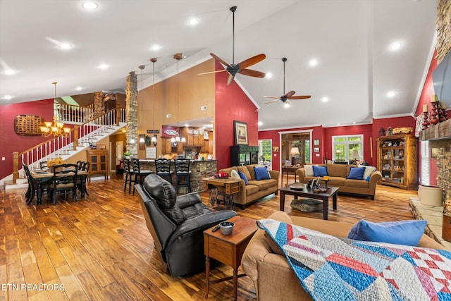 living room featuring ornate columns, ceiling fan with notable chandelier, crown molding, wood-type flooring, and high vaulted ceiling