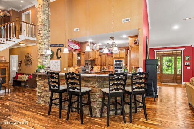 kitchen featuring kitchen peninsula, hardwood / wood-style floors, decorative columns, and ornamental molding