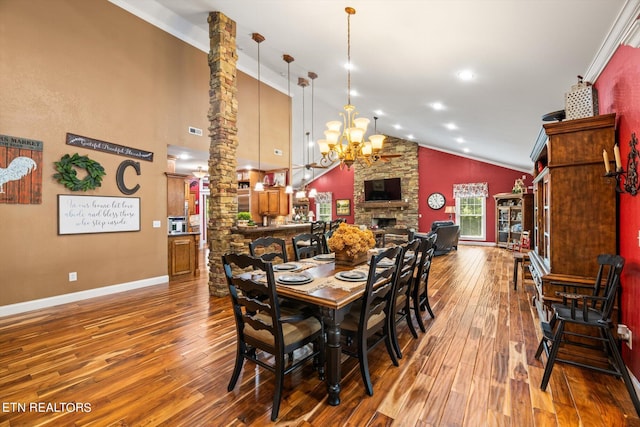 dining space featuring decorative columns, hardwood / wood-style flooring, high vaulted ceiling, a notable chandelier, and a fireplace