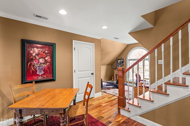 dining space with wood-type flooring, lofted ceiling, and ornamental molding