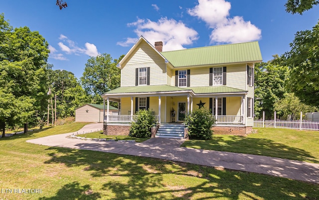 country-style home featuring a porch, an outbuilding, and a front yard