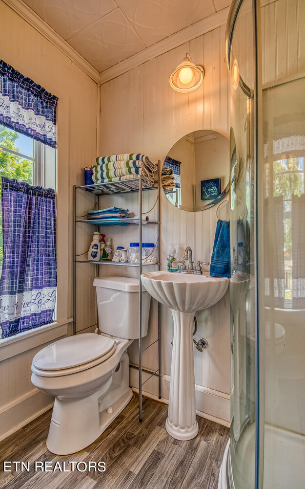 bathroom featuring wood-type flooring, wooden walls, toilet, and crown molding