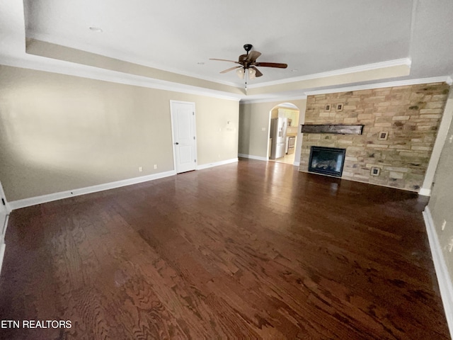 unfurnished living room featuring ornamental molding, a tray ceiling, ceiling fan, dark wood-type flooring, and a stone fireplace