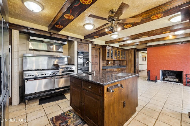 kitchen featuring a center island with sink, sink, dark stone countertops, light tile patterned floors, and a textured ceiling