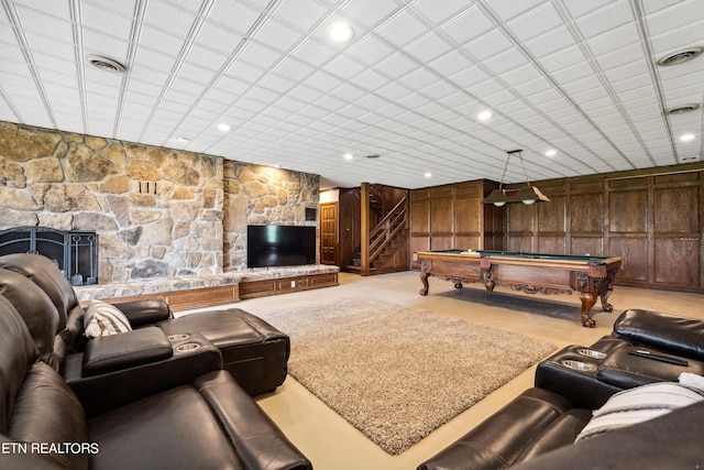 living room featuring wood walls, a stone fireplace, and pool table