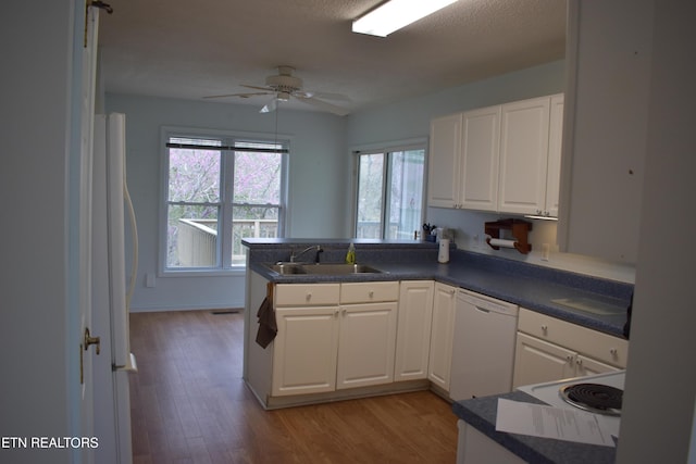 kitchen featuring white dishwasher, a sink, ceiling fan, a peninsula, and wood finished floors