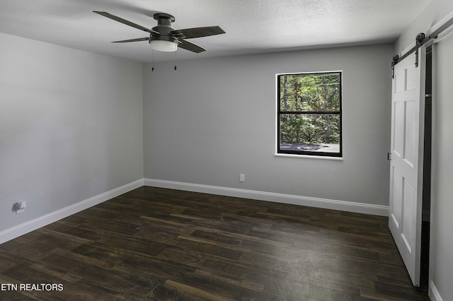 unfurnished bedroom with ceiling fan, a barn door, dark hardwood / wood-style flooring, and a textured ceiling