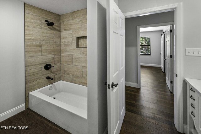 bathroom with hardwood / wood-style flooring, vanity, and tiled shower / bath