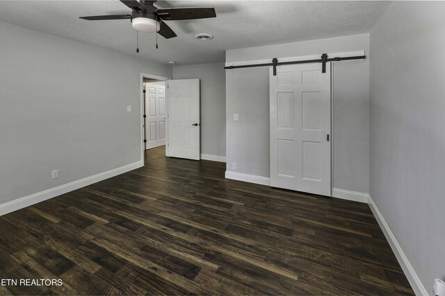 unfurnished bedroom featuring a textured ceiling, ceiling fan, a barn door, and dark wood-type flooring