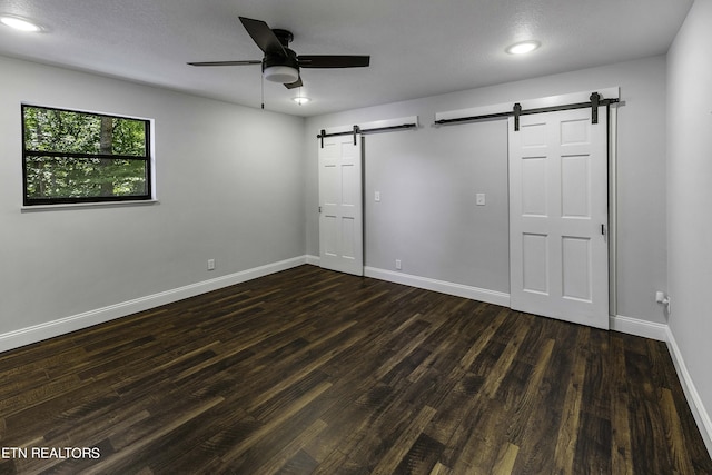 spare room featuring a barn door, ceiling fan, and dark wood-type flooring