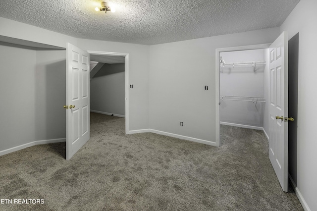 unfurnished bedroom with dark colored carpet, a spacious closet, and a textured ceiling