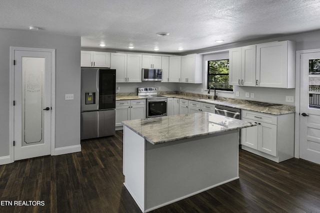 kitchen featuring white cabinets, appliances with stainless steel finishes, a kitchen island, and light stone counters