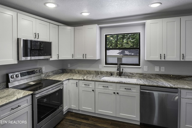 kitchen with sink, stainless steel appliances, light stone counters, a textured ceiling, and white cabinets