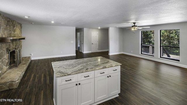 kitchen with white cabinetry, a fireplace, ceiling fan, and light stone countertops