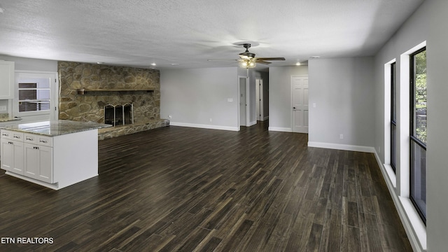 unfurnished living room with a textured ceiling, ceiling fan, a fireplace, and dark wood-type flooring