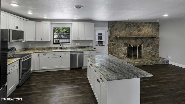 kitchen featuring white cabinets, stainless steel appliances, a stone fireplace, and sink