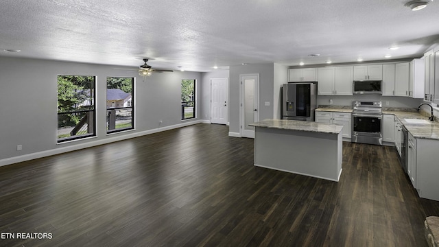 kitchen with appliances with stainless steel finishes, light stone counters, sink, white cabinetry, and a kitchen island