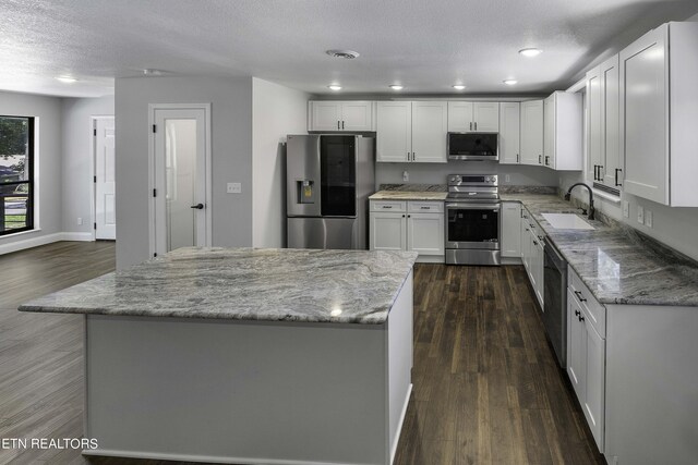 kitchen with white cabinets, stainless steel appliances, light stone counters, and sink