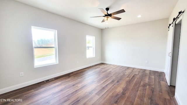 unfurnished bedroom with dark wood-style floors, a barn door, multiple windows, and baseboards