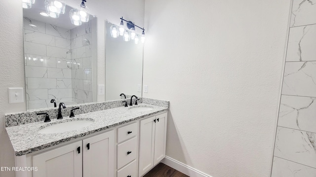 bathroom featuring a textured wall, double vanity, tiled shower, and a sink