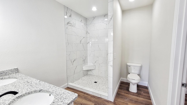 bathroom featuring toilet, a sink, wood finished floors, tiled shower, and baseboards