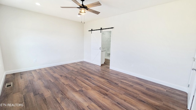 spare room featuring dark wood finished floors, visible vents, a barn door, ceiling fan, and baseboards