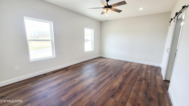 unfurnished bedroom featuring a barn door, visible vents, baseboards, dark wood-style flooring, and recessed lighting