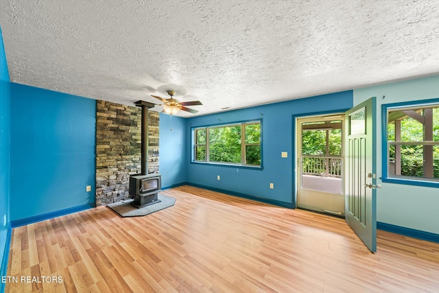 unfurnished living room with ceiling fan, a wood stove, a textured ceiling, and light hardwood / wood-style flooring