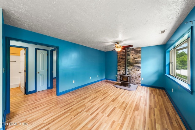 unfurnished living room with a textured ceiling, ceiling fan, light hardwood / wood-style floors, and a wood stove