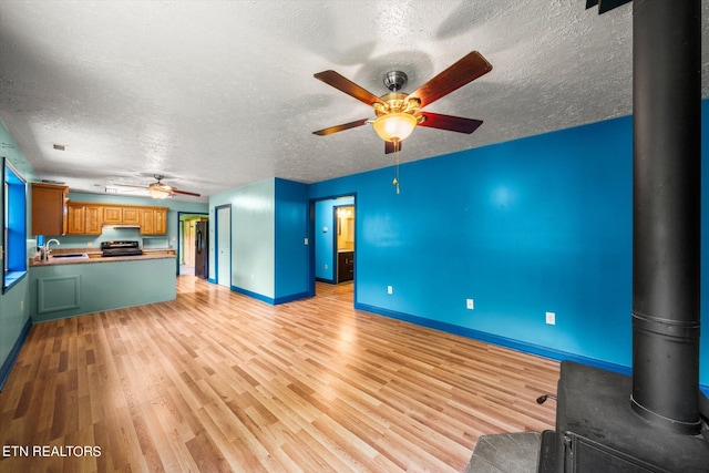 unfurnished living room featuring ceiling fan, a wood stove, a textured ceiling, and light wood-type flooring