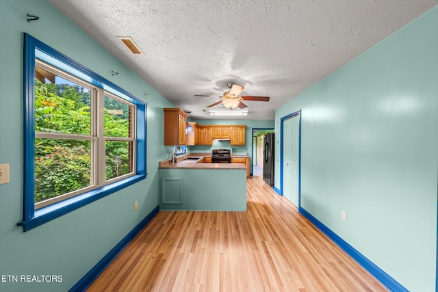 kitchen featuring a textured ceiling, black refrigerator, kitchen peninsula, light wood-type flooring, and electric range