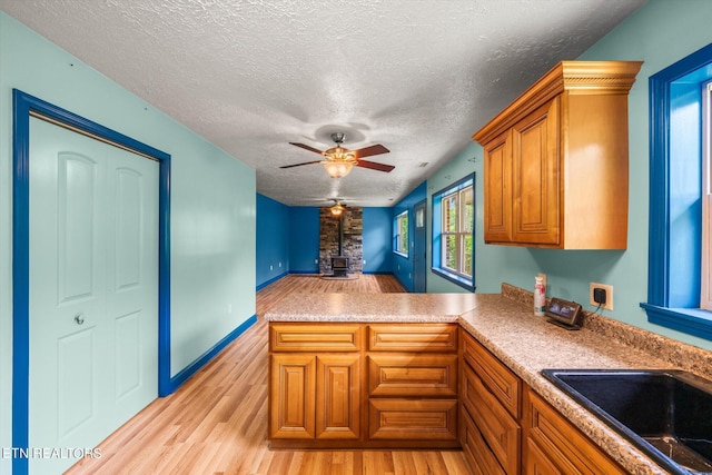 kitchen featuring ceiling fan, kitchen peninsula, sink, light wood-type flooring, and a textured ceiling