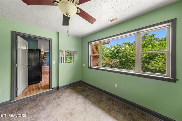 unfurnished bedroom with ceiling fan, a textured ceiling, and black fridge