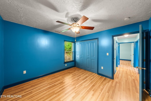 unfurnished bedroom with ceiling fan, light hardwood / wood-style floors, a textured ceiling, and a closet