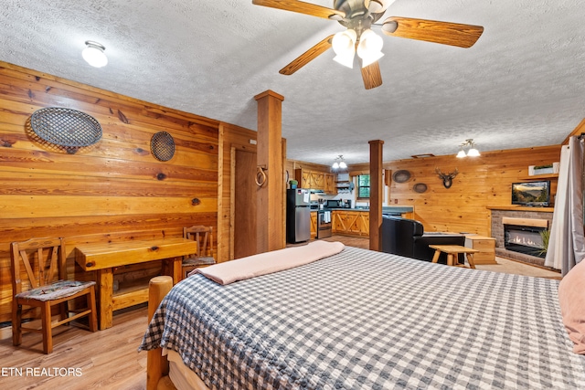 bedroom featuring a textured ceiling, ceiling fan, light hardwood / wood-style floors, stainless steel refrigerator, and wood walls