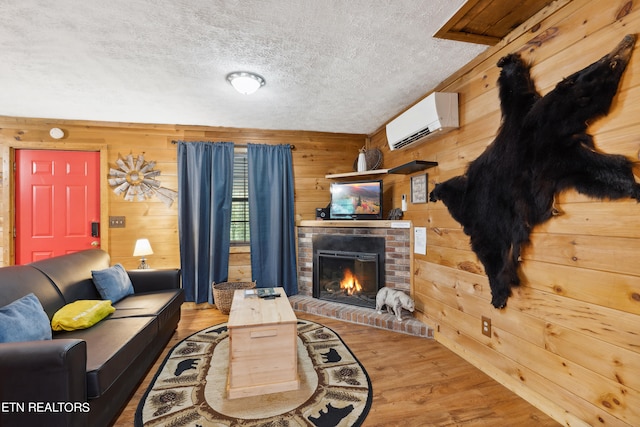 living room featuring a brick fireplace, a textured ceiling, a wall unit AC, hardwood / wood-style flooring, and wood walls